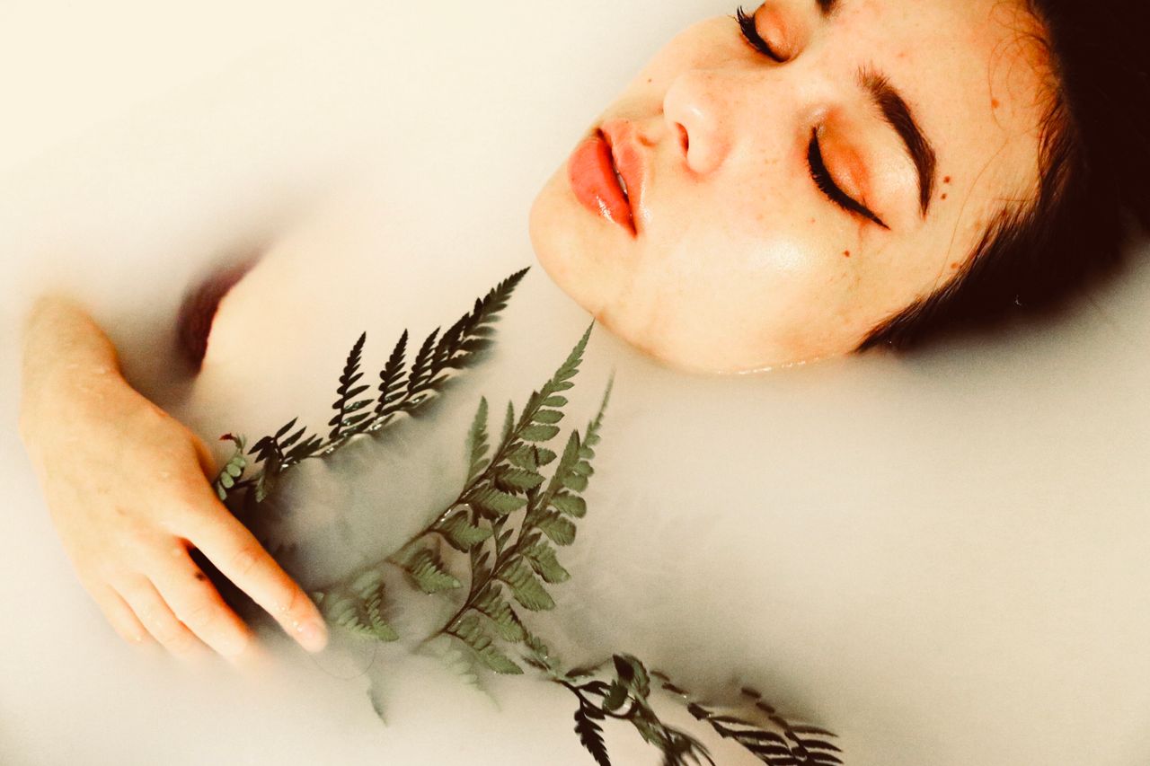 home-img A tranquil portrait of a woman in a milk bath holding a fern leaf, conveying beauty and relaxation.