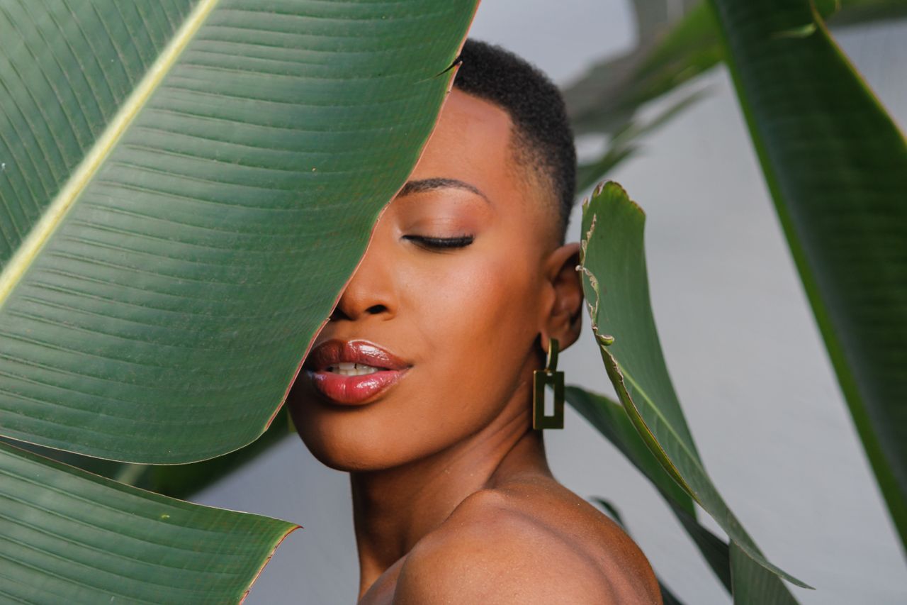 gallery-04 A serene portrait of a woman with closed eyes, framed by lush tropical leaves.