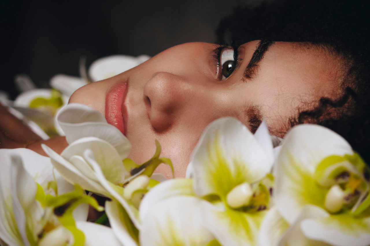 gallery-05 A serene portrait of a woman surrounded by white and green orchids in close-up.
