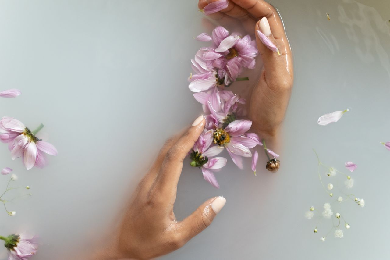 Top view of anonymous female with manicured hands touching delicate flowers while taking bath with white soapy water