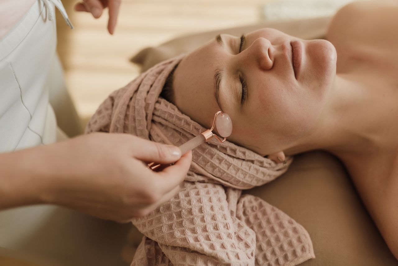 gallery-01 A woman with closed eyes enjoying a peaceful facial roller treatment in a spa setting.